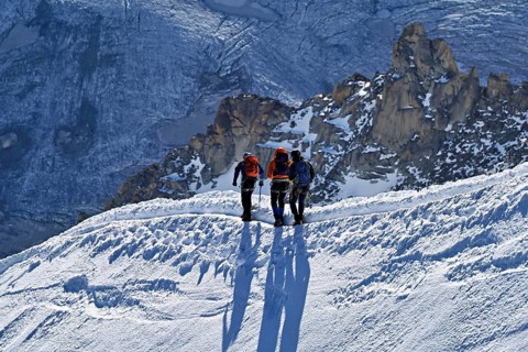 Three ascended mountaineers run across a snow-covered mountain ridge, Aiguille du Midi,