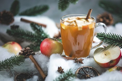 A glass of apple punch and apple pieces in a wintery setting