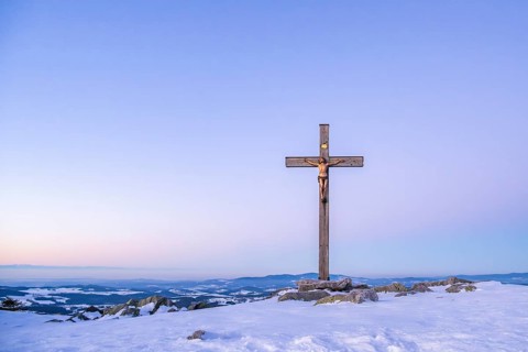 Christian cross on the peak of Mount Lusen with the view over the hills of the bavarian forest at