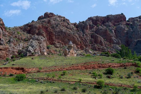 Church on green meadow against dramatic rocky backdrop under blue sky, Noravank monastery, Surb