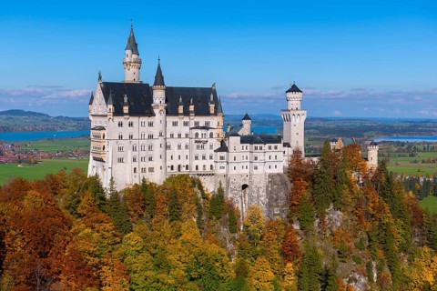 Impressive Neuschwanstein Castle in autumn landscape, surrounded by colorful trees and under blue