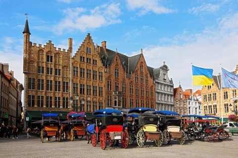Historic houses on the market square in the old town of Bruges with horse-drawn carriages, Grote