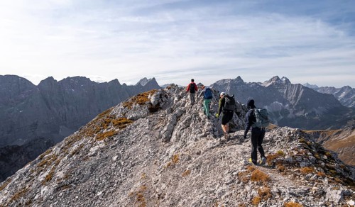 Hikers on the summit ridge of the Gamsjoch, behind rock faces of the Laliderer Spitze, eastern