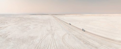 Aerial view, two off-road cars driving on a salt pan, arid landscape, Botswana