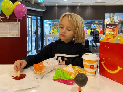Interior view, child, boy, 7 years, blonde, eating Happy Meal, children's menu, at McDonald's