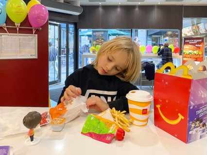 Interior view, child, boy, 7 years, blonde, eating Happy Meal, children's menu, at McDonald's