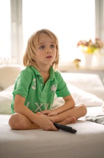 Child, boy, 7 years old, blonde, sitting on sofa, with remote control in hand, watching TV,