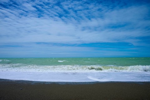 Wavy beach with calm sky in the background, Tuhawaiki Point Lighthouse or Jack's Point Lighthouse,