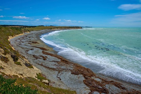 Long stretch of coastline with wavy sea and blue sky, Tuhawaiki Point Lighthouse or Jack's Point