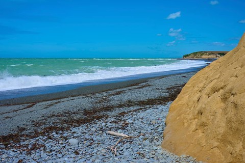 Rocky beach with waves and blue sky, Tuhawaiki Point Lighthouse or Jack's Point Lighthouse,
