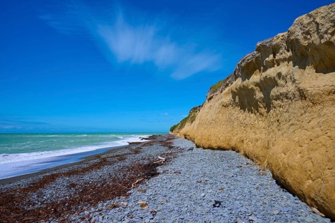 Cliff with pebble beach and blue sky on a sunny day, Tuhawaiki Point Lighthouse or Jack's Point
