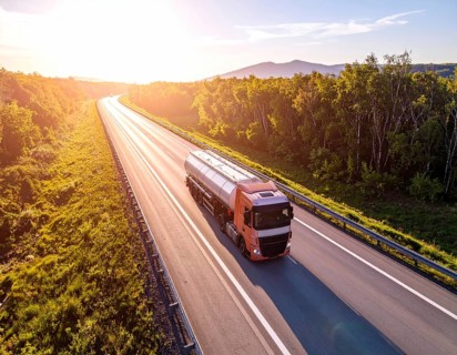 Petrol cargo truck lorry tanker driving on highway hauling oil products at sunrise, wide hilly