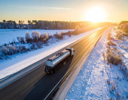 Petrol cargo truck lorry tanker driving on highway hauling oil products at sunrise, wide snowy