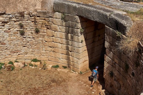 Visitor walks through huge stone gate, Mycenaean domed tomb, archaeological site, UNESCO World