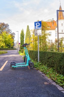 An electric scooter is parked on a sidewalk next to a parking sign against an autumn backdrop,