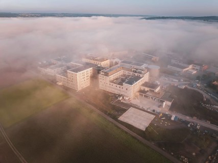 Industrial buildings seen from the air in morning fog, surrounded by natural landscape at dusk, new