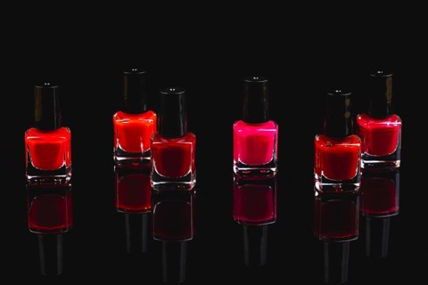 Six bottles of nail polish in shades of red and pink on a black surface with reflection