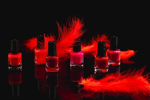 Nail polish bottles in shades of red and pink with red feathers on a black surface with reflection