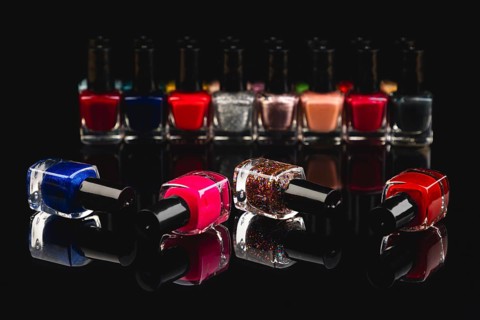 Different nail polish bottles in intense colors on a black surface with reflection