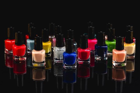 Different bottles of colored nail polishes with reflection on black background