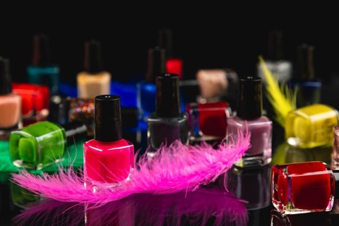 Colourful nail polish bottles and coloured feathers on black surface with reflection