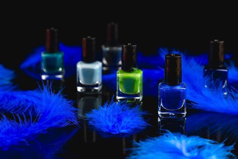 Nail polish bottles in shades of blue and green with blue feathers on a black surface with