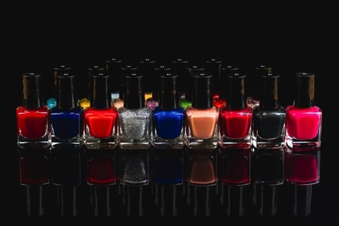 A variety of nail polish bottles in different colors with reflections on a black background