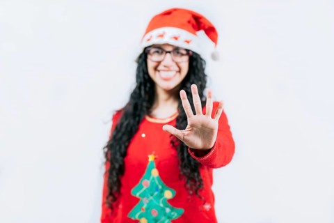Smiling girl in Christmas sweater counting five. Funny girl in a Christmas hat counting five,