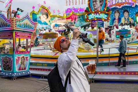 Influencer with live camera and beer in front of a fairground ride. Cannstatter Volksfest at the