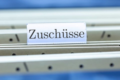 (Photomontage) Sign with the inscription ZUSCHÜSSE on a suspension file index