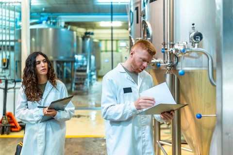 Employees wearing lab coats inspecting production process and quality control data inside a modern