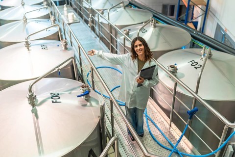 Woman wearing a white lab coat and holding a clipboard, standing on a metal gangway, showing a row