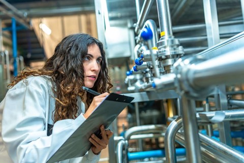 Woman in a white coat diligently checking and documenting the status of stainless steel pipes and