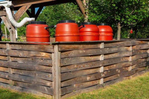Reddish brown plastic water butts collecting and storing rain water from white plastic downspout in