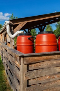 Reddish brown plastic water butts collecting and storing rain water from white plastic downspout in