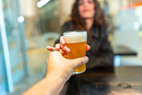 Hand holding a refreshing glass of craft beer, presenting it to a woman in a bar, representing