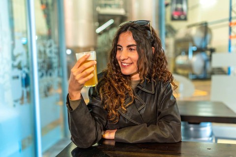 Woman in a leather jacket smiling and savoring a glass of craft beer at a modern brewery bar,