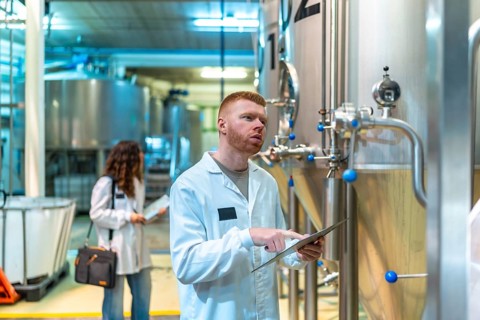 Brewery quality control team inspecting industrial fermentation tanks, a technician monitoring data
