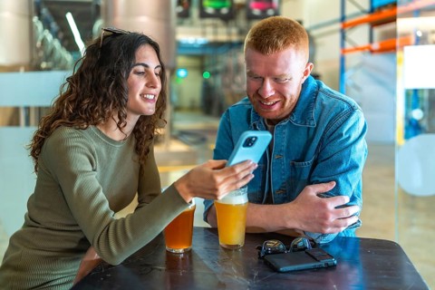 Young couple sitting at a table in a brewery or beer factory, having a conversation and sharing