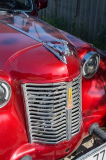Front of a shiny red vintage car with a striking emblem in the sun, Moskvich 401, Armavir province,
