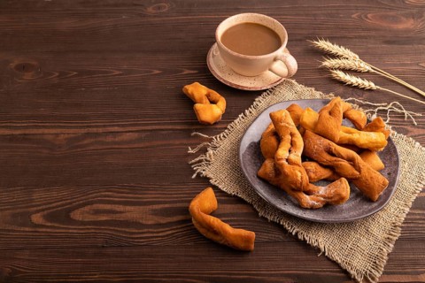 Crunchy biscuit Brushwood cookies sprinkled with powdered sugar on brown wooden background and