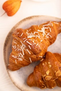 Croissant on blue plate on white wooden background and orange linen textile, cup of coffee, side