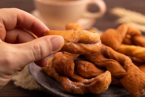 Crunchy biscuit Brushwood cookies with hand sprinkled with powdered sugar on brown wooden
