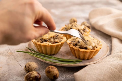 Tartlets with meat and cheese with hand on brown concrete background and linen textile. side view,