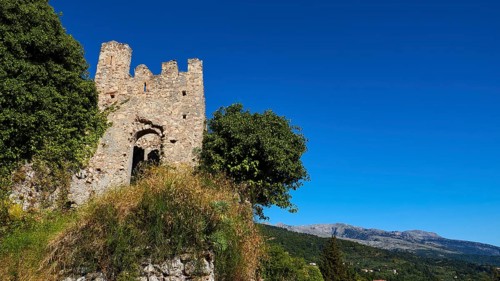 Ancient ruined tower with neighbouring trees against a picturesque blue sky and mountain backdrop,