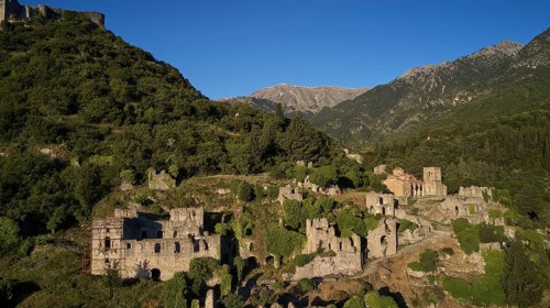 Drone shotRuins and buildings on a hill surrounded by green mountain landscape, including the