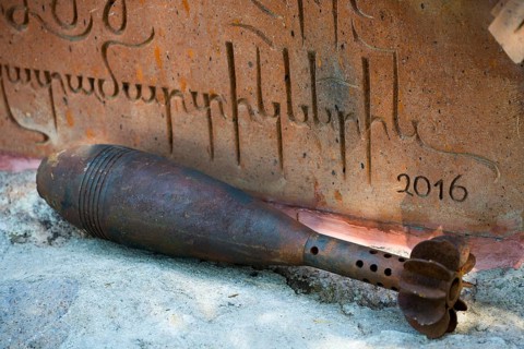 Rusty grenade lies in front of an engraved memorial plaque with the year 2016, mortar shell,