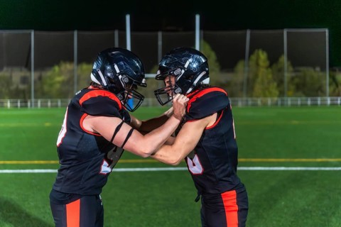 Two american football players in black and orange uniforms collide in a gritty close up on green