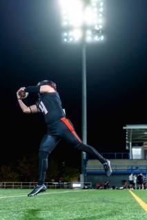 American football player in black and orange uniform catching an airborne football on a green turf
