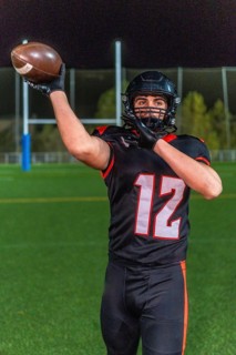 American football player in helmet and number 12 uniform holds the ball up on a green grass field